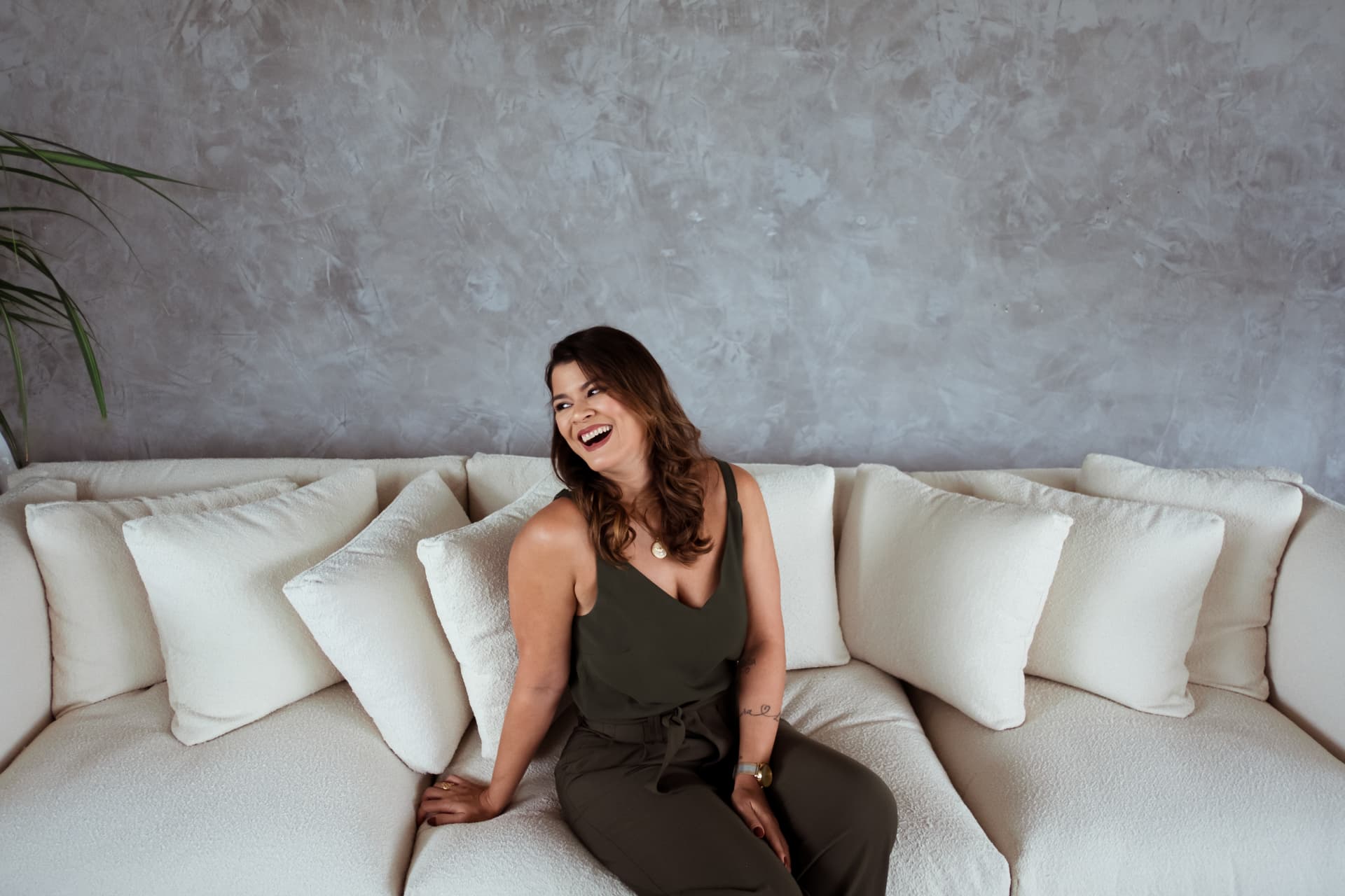 Juliana rindo, sentada em um sofá claro